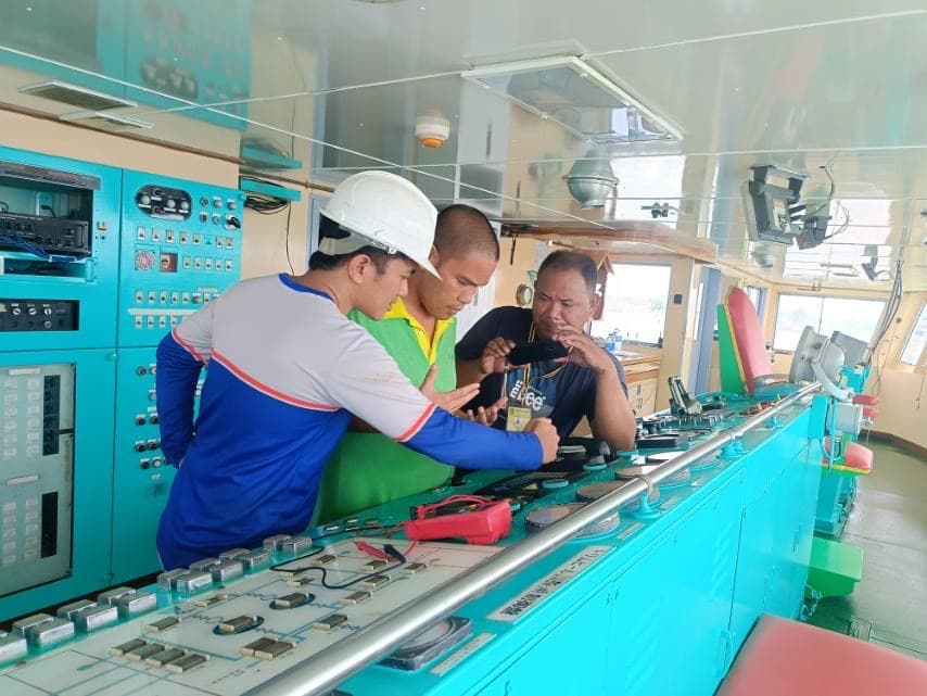 Technicians verifying instrumentation on a ship bridge control console